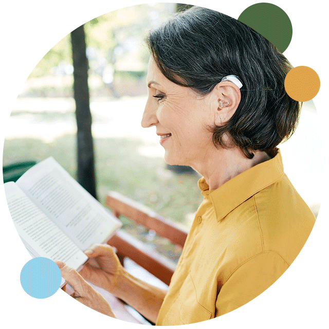 Woman outsite reading a book with hearing aid